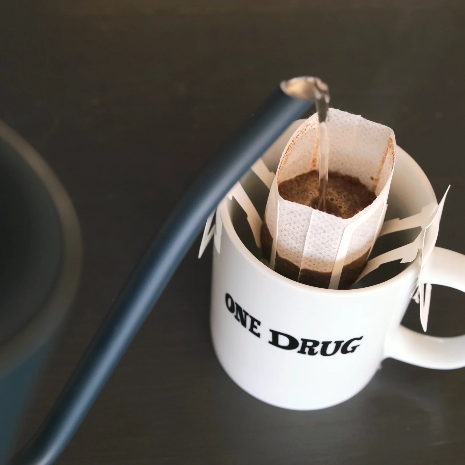 Hot water pouring into a drip bag filter set over a white One Drug mug
