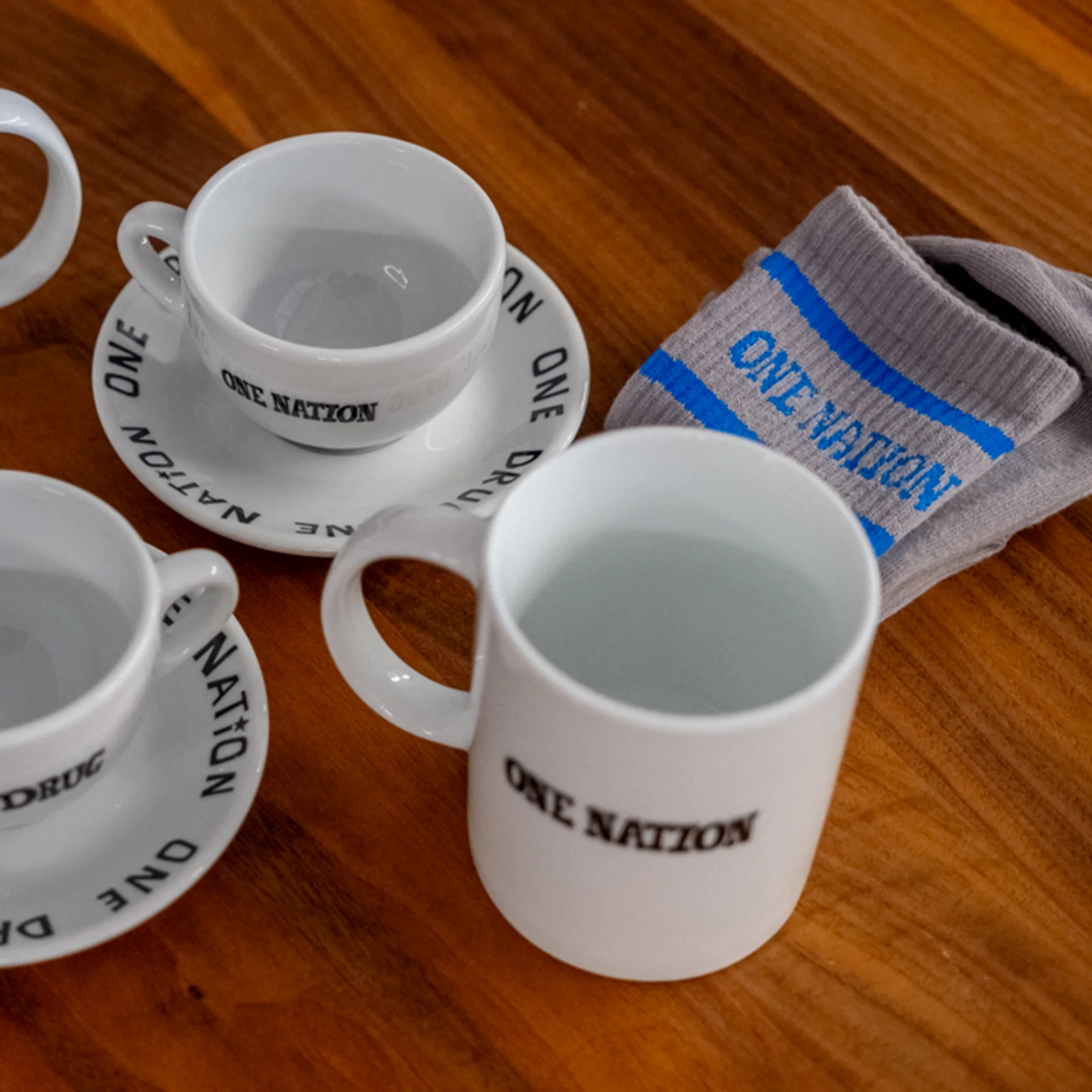 White One Nation espresso cups, a mug and grey One Nation socks on a wooden table